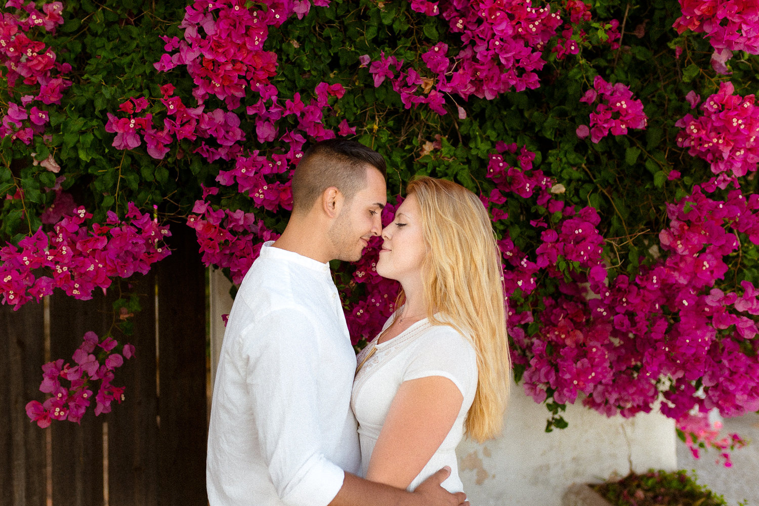 Couple embracing in front of vibrant flowers during an Algarve engagement session with bougainvillea